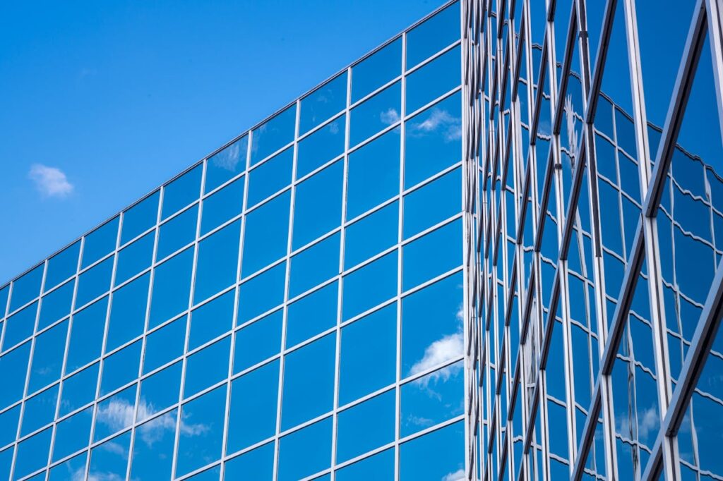 Contemporary glass building with a reflective facade showing a blue sky and clouds.