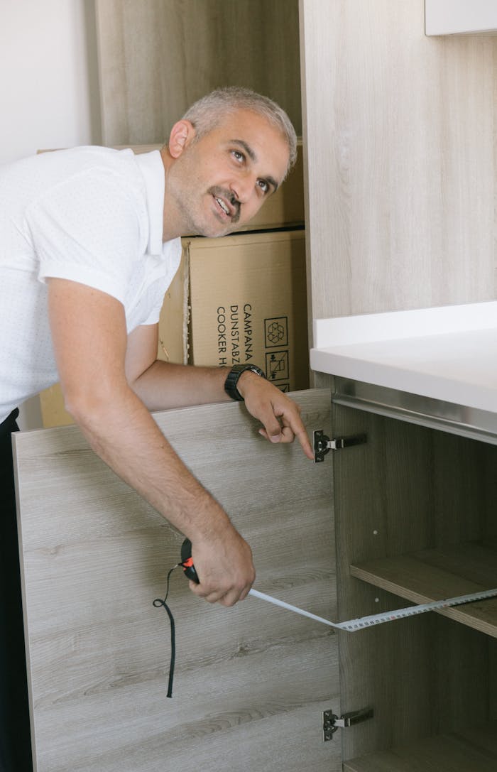 Man in white shirt measuring kitchen cabinet with tape in Istanbul apartment. Ideal for real estate or DIY themes.